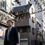 都市部の公園で、多数のドバトが留まる電線や木の下を歩く日本人男性。宝くじのポスターの前を通り、空から何かが落ちてくる様子。